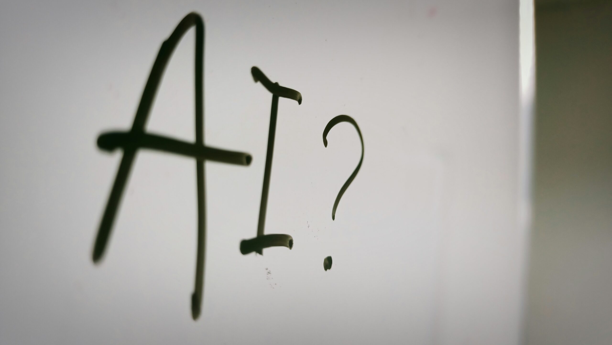 Close-up of the word “AI?” handwritten on a whiteboard, symbolizing curiosity and conversation around artificial intelligence.